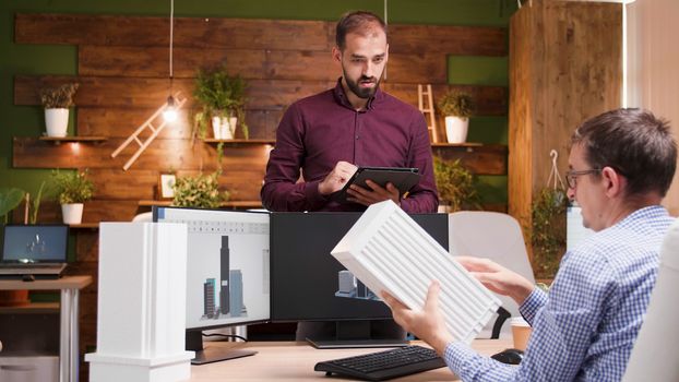 Architect sitting at his office explaning his assistant the building concept for the city.