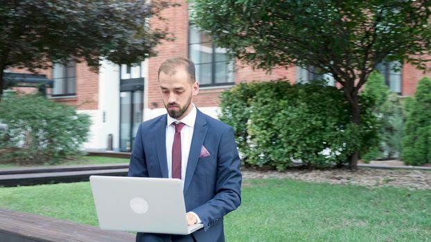 Manager in formal suit typing on the laptop, working outdoor in the city. Business on the go