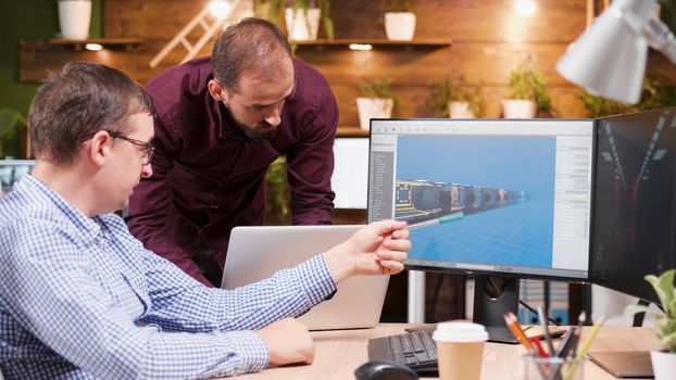 Graphic designer in game industry sitting at his office showing his assistant new gaming graphics.