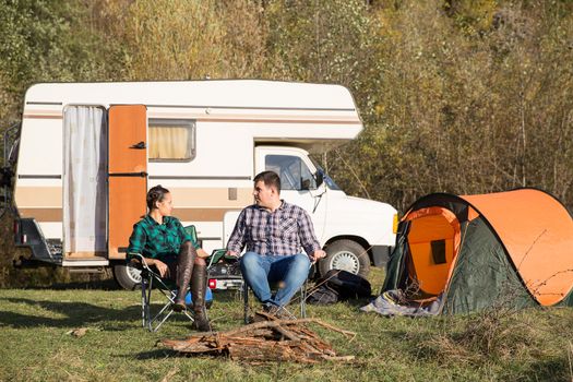 Couple relaxing together in campsite in the mountains with their retro camper van in the background.