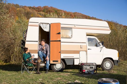 Man sitting on the stairs of his retro camper van in the mountains and talking with his girlfriend.