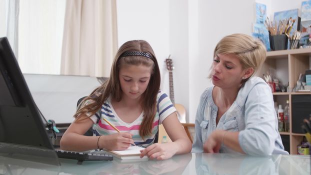 Teenage girl drawing something in her notebook and her mother talks to her. Mom and her daughter at a desk.