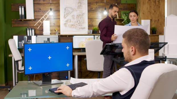 Creative architect working on computer with blue screen. Architects holding blue prints.