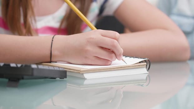 Young girl's hands drawing something in a notebook. Girl uses a pencil to draw something on a paper.