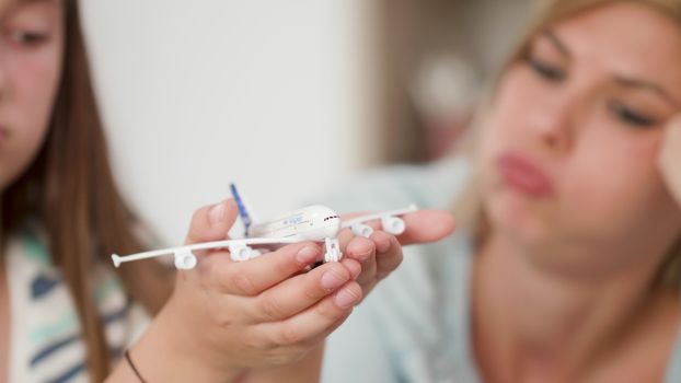 Teenage girl holds a toy plane in her palm and show it to her mom. family dreaming of a trip together.