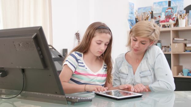 Teenage girl swiping the screen of a tablet while her mother looks at the screen. Showing pictures to her mother.