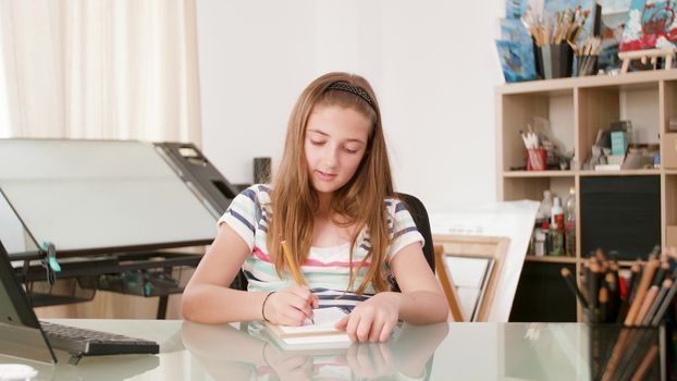 Teenage girl draws something in her notebook and talks to herself. Girl is inspired and uses a pencil to draw something.