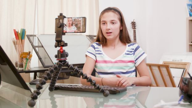 Teenage girl streaming a live video for her followers. Vlogger talking to her followers. Smartphone on a tripod.