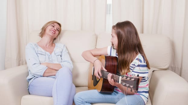 Teenage girl plays a song on the guitar to her mother. Mother is enjoying her daughter singing.