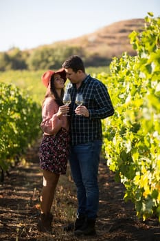 Happy young couple embracing each other in the grape fields holding glasses of wine. Happy young couple in a vineyard looking at each other.