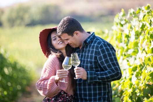 A young couple in love in the vineyards holding glasses of wine.