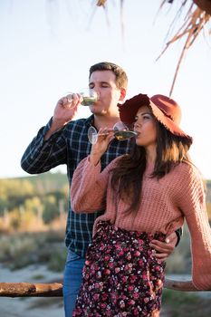 Couple in love drinking wine together with sunset light behind it on a wooden ponton in a big vine yard with a lake