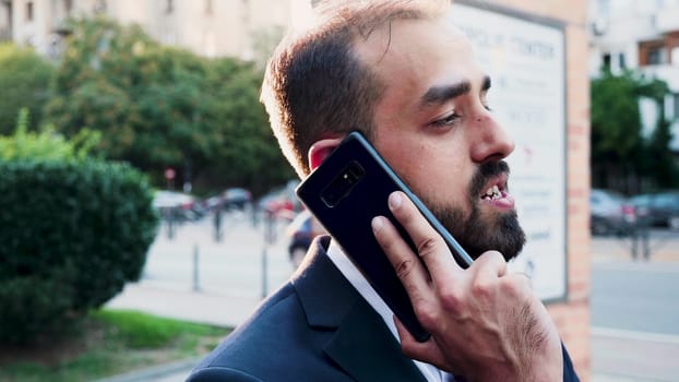 Caucasian man in business suit on the phone outdoor in the city. Lens flares from behind. Slow motion footage