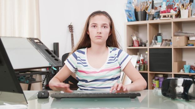 Portrait of a teenage girl typing a text on her computer. Typing a e mail on her keyboard looking at the camera.