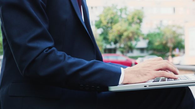 Manger in business suit typing on laptop keyboard outdoor in the city, close up