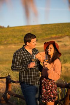 Happy young couple looking at each other and smiling while enjoying a glass of wine in a vineyard.