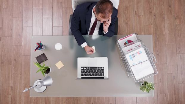 Top view of businessman in suit talking on the phone and making notes sitting at his office.