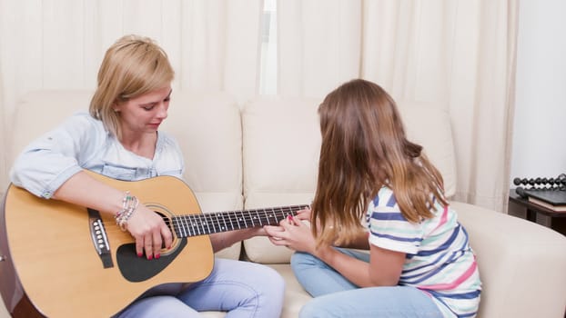 Daughter showing to her mother how to play a song on the guitar. Learning to play an acoustic guitar.