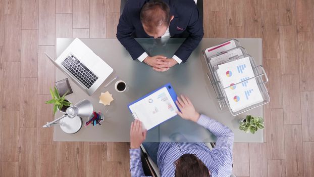 Top view of businessman in suit shaking hands with a manager and reading graphs form a clipboard.