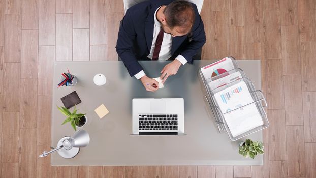 Top view of businessman in suit talking on the phone and taking notes sitting at his office.