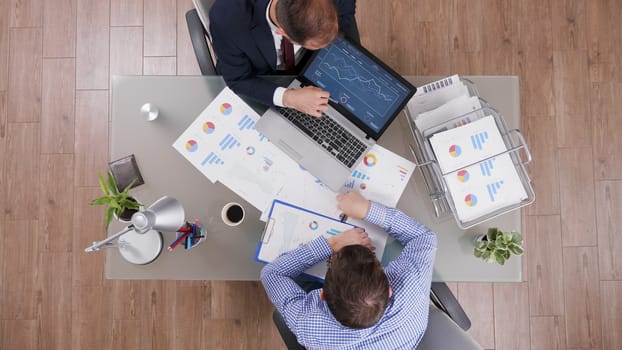 Businessmen working together at office desk and checking charts from laptop.