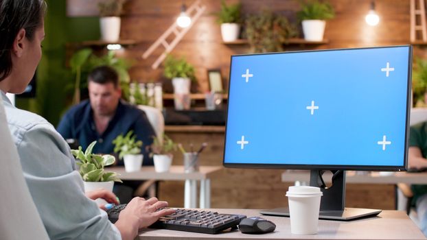 Woman typing on a computer with a blue screen mock-up in modern and cozy office