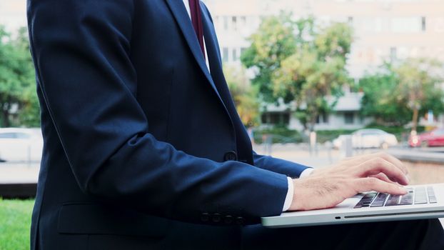 Businessman hands typing on laptop keyboard outdoor in the city, close up