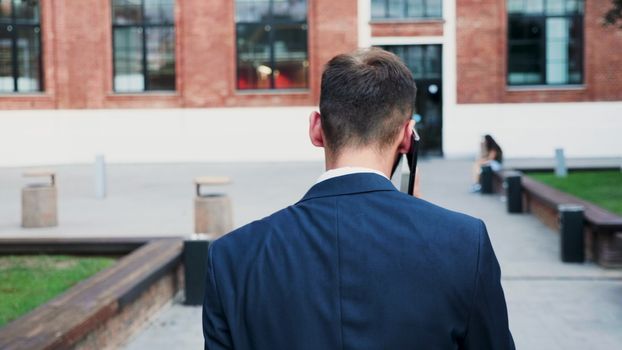 Man in business suit walking in the city and talking on the phone, back view slow motion tracking shot