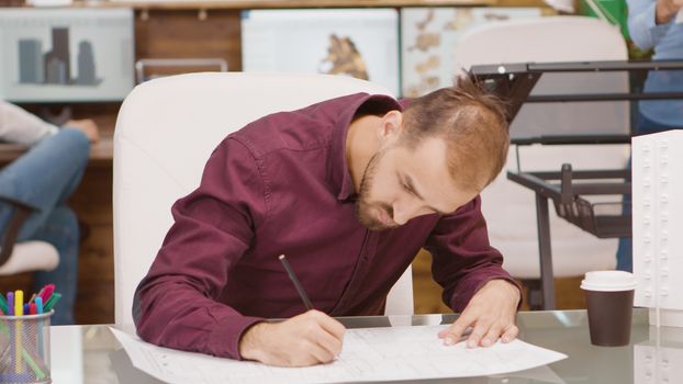 Bearded young architect drawing the project of a building on blue prints. 3D print model