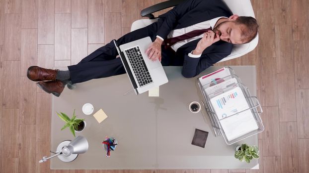 Top view of businessman in suit sitting relaxed at his office with his feet on and working on laptop.