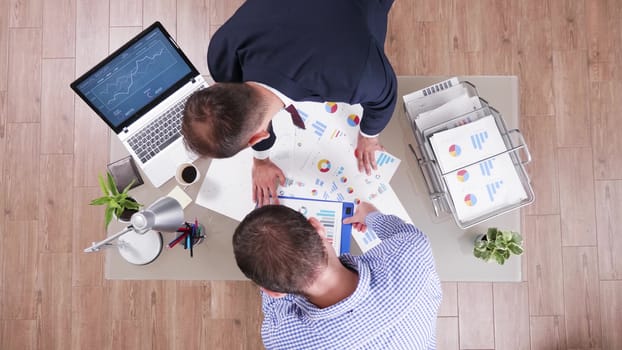 Top view of two businessman checking charts from different files and shaking hands in the office.
