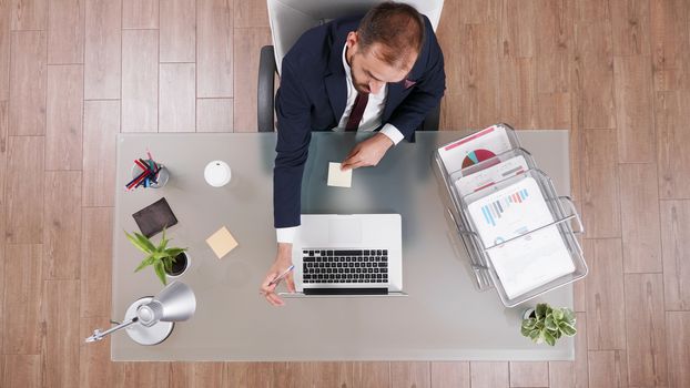 Top view of businessman in suit talking on the phone and taking notes sitting at his office.