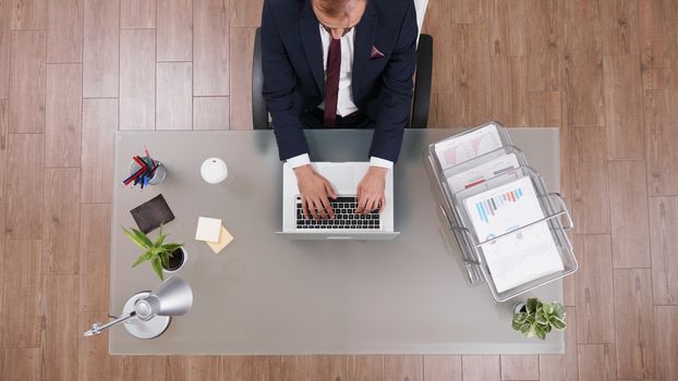 Top view of businessman in suit typing on laptop with a cup of coffee next to him