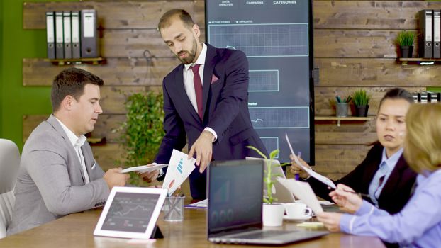 Bearded businessman in suit giving his team to analyze charts in the conference room.