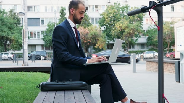 Man in business suit typing on the laptop outdoor of his office in the city. Working on the go concept
