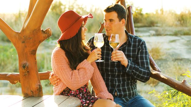 Beautiful caucasian couple in sun flares clinking glasses with white wine.