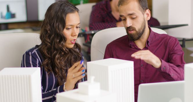 Businessman and creative designer working on 3D printed models of buildings in modern office space
