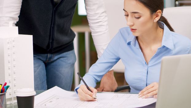 Construction engineer talking with female architect and drawing on blue print. Building model.