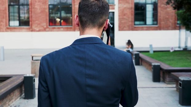 Back view of businessman having on conversation on the phone, slow motion. He is outdoor in the busines distric