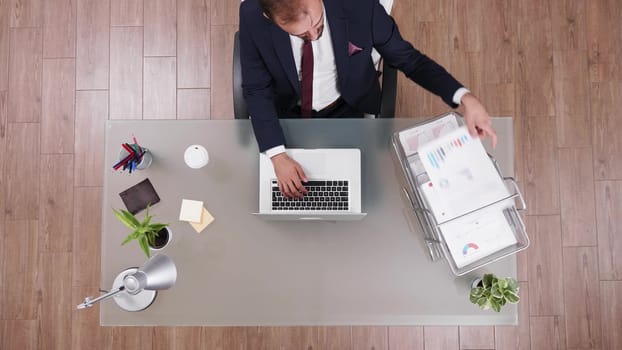 Top view businessman typing and reading data from a chart in his corporate office.