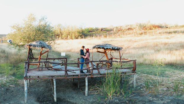 Beautiful couple clinking glasses with wine on a pontoon in a rural area, aerial drone shot