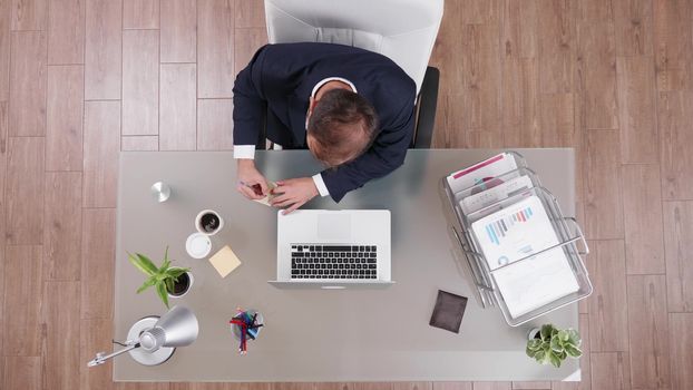 Caucasian businessman typing on his laptop and making notes on sticky papers, top view