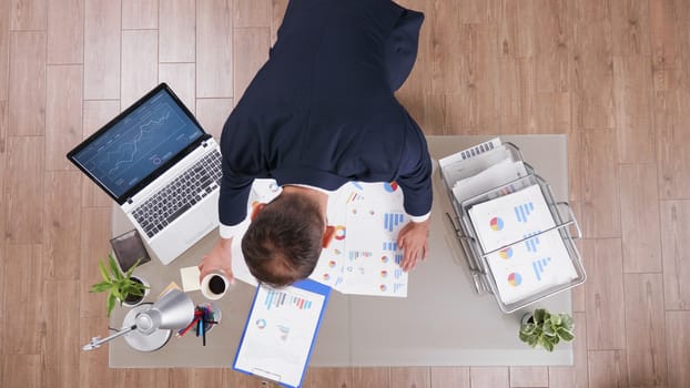 Top view of businessman in suit taking a sip of coffee and analysing documents in his office.