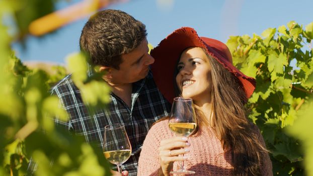 Close up of gorgeous couple embracing each other while holding glasses of wine in hands.