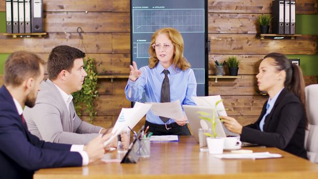 Caucasian executive female giving her young team new charts to study. Important business meeting.