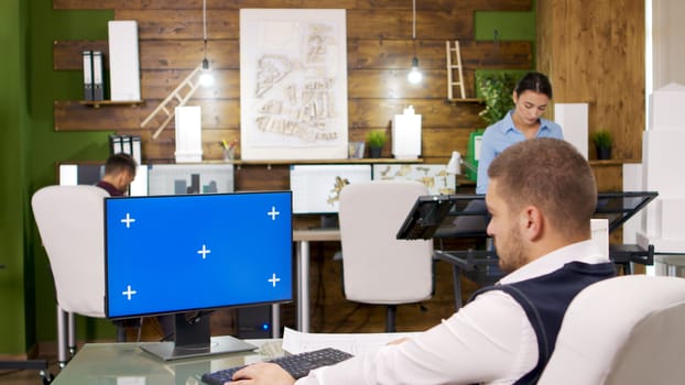 Young architect working on a computer with blue screen. Collegues working in the background.