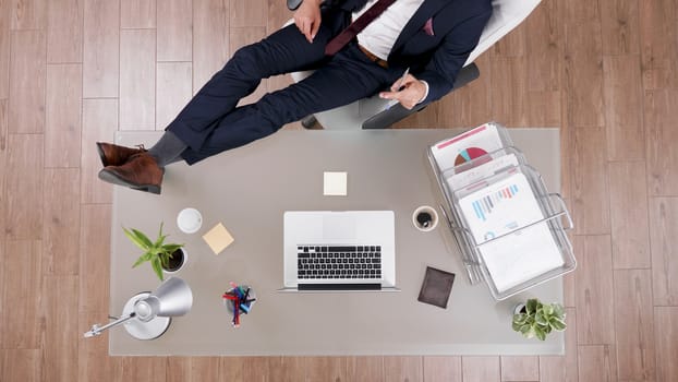 Top view of businessman in suit staying relaxed with feet on his office desk. Modern looking office.