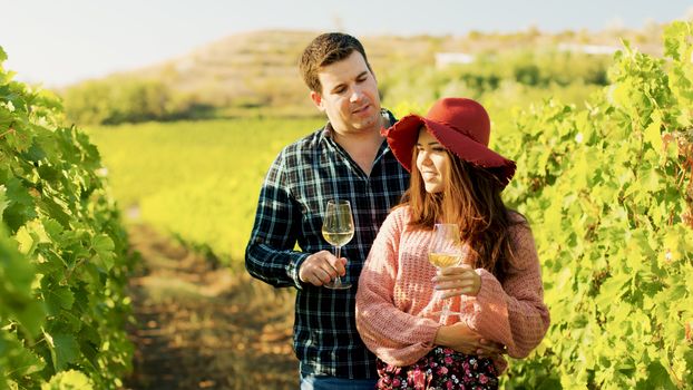 Gorgeous couple embracing each other while holding glasses of wine in hands.
