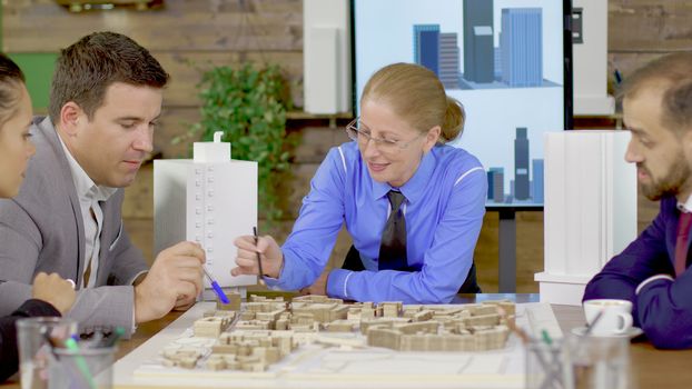 Middle age female architect in a meeting with his team in the conference room, Team of archtects. Mini town.