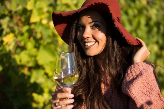 Smiling beautiful woman in a vineyard holding a glass of wine and looking at the camera.